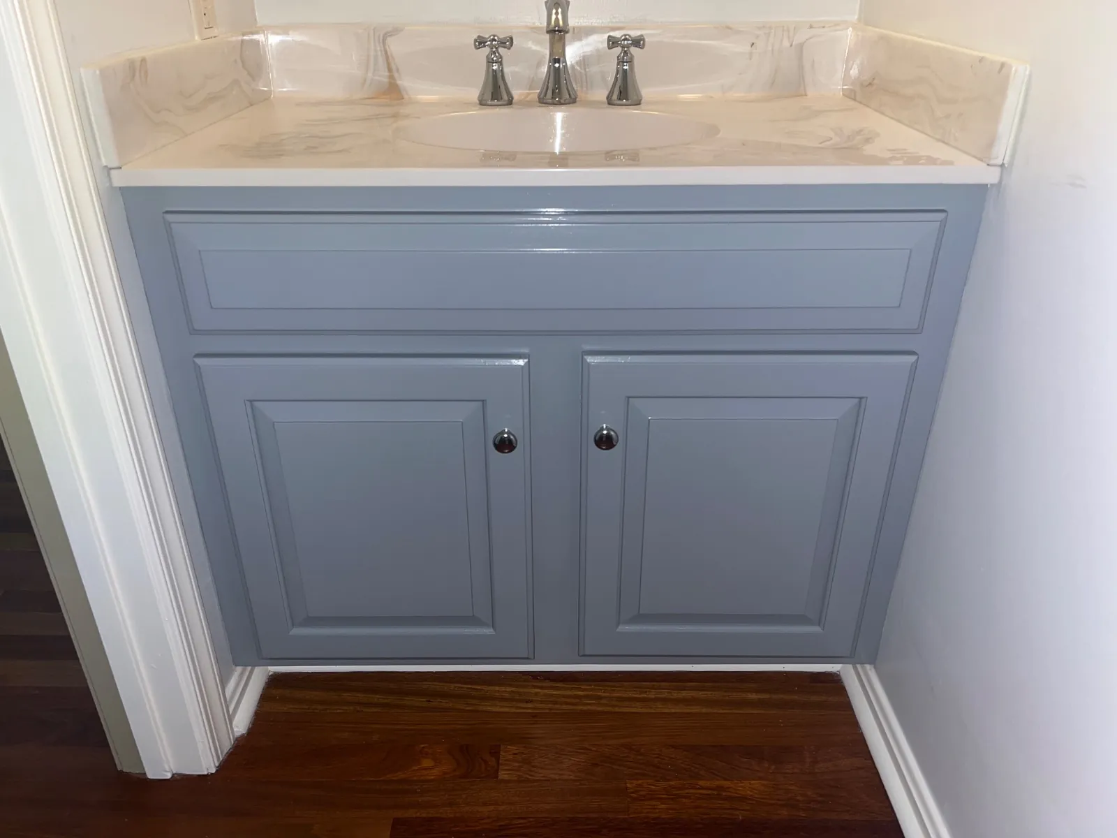 Bathroom vanity painted blue-gray, with chrome knobs and a marble-look top