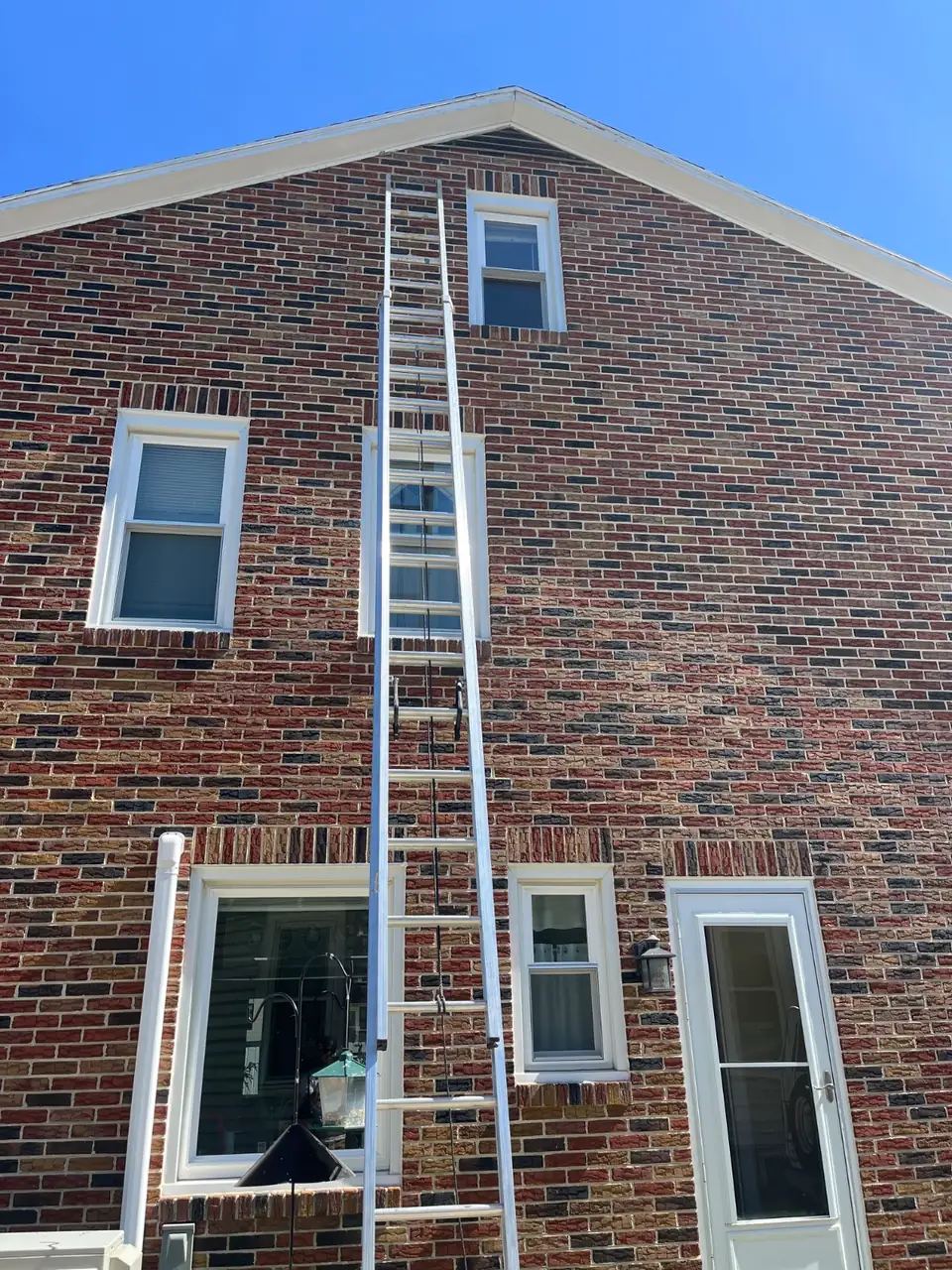 Aluminum extension ladder set against the brick gable wall of a house with white window trim