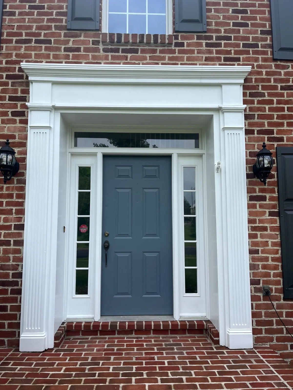 Slate blue front door in a white entry surround with fluted pilasters on a red brick house