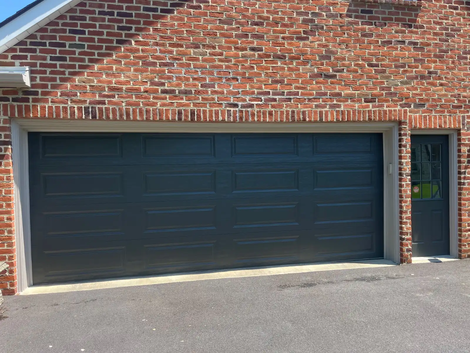 Double garage door after painting, dark charcoal, with a matching side door in a red brick wall