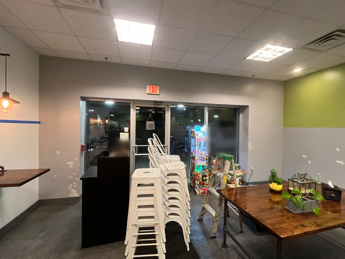 Shop walls before painting, light gray with white patch spots, stools stacked by the front doors