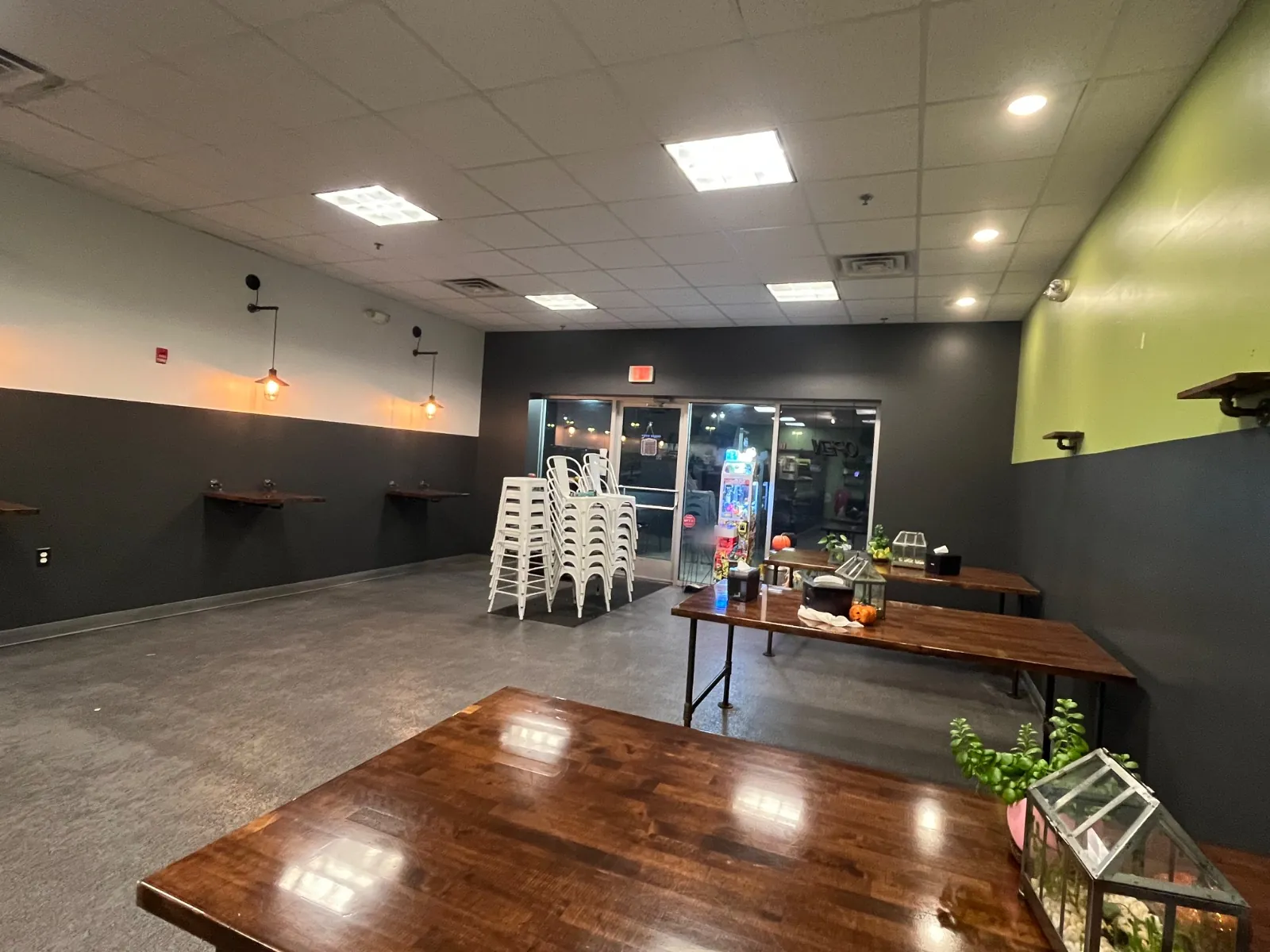 Shop seating area with charcoal lower walls, a lime green wall, wood tables and stacked white stools