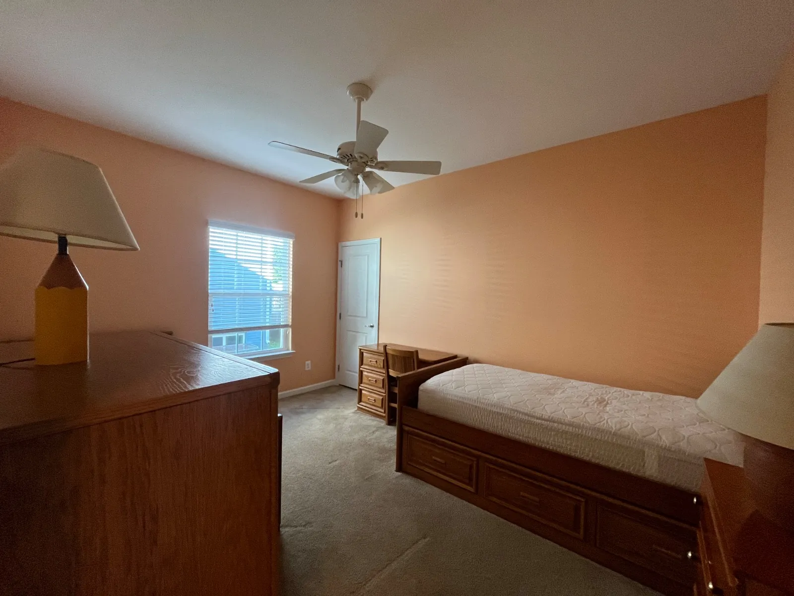 Bedroom with peach walls, a white ceiling fan, a twin bed and a small wood desk