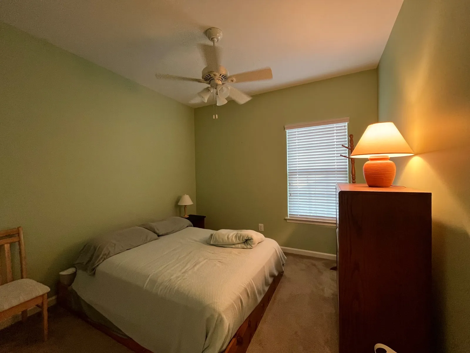 Bedroom with sage green walls, a white ceiling fan, a bed and a wood dresser