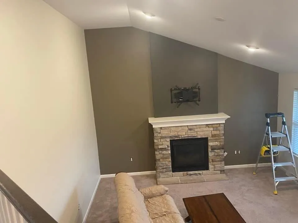 Living room with taupe and gray accent walls behind a stone fireplace, a stepladder at the right